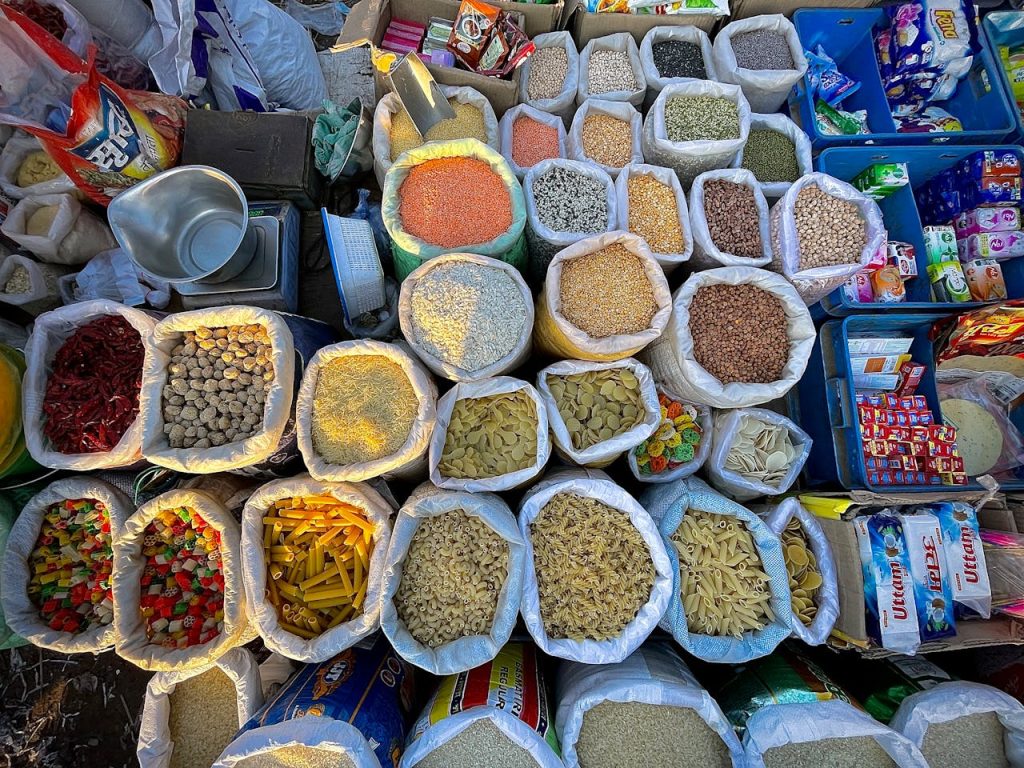 Top-down view of colorful market goods including spices, grains, and pasta in bags, showcasing a vibrant array of choices.